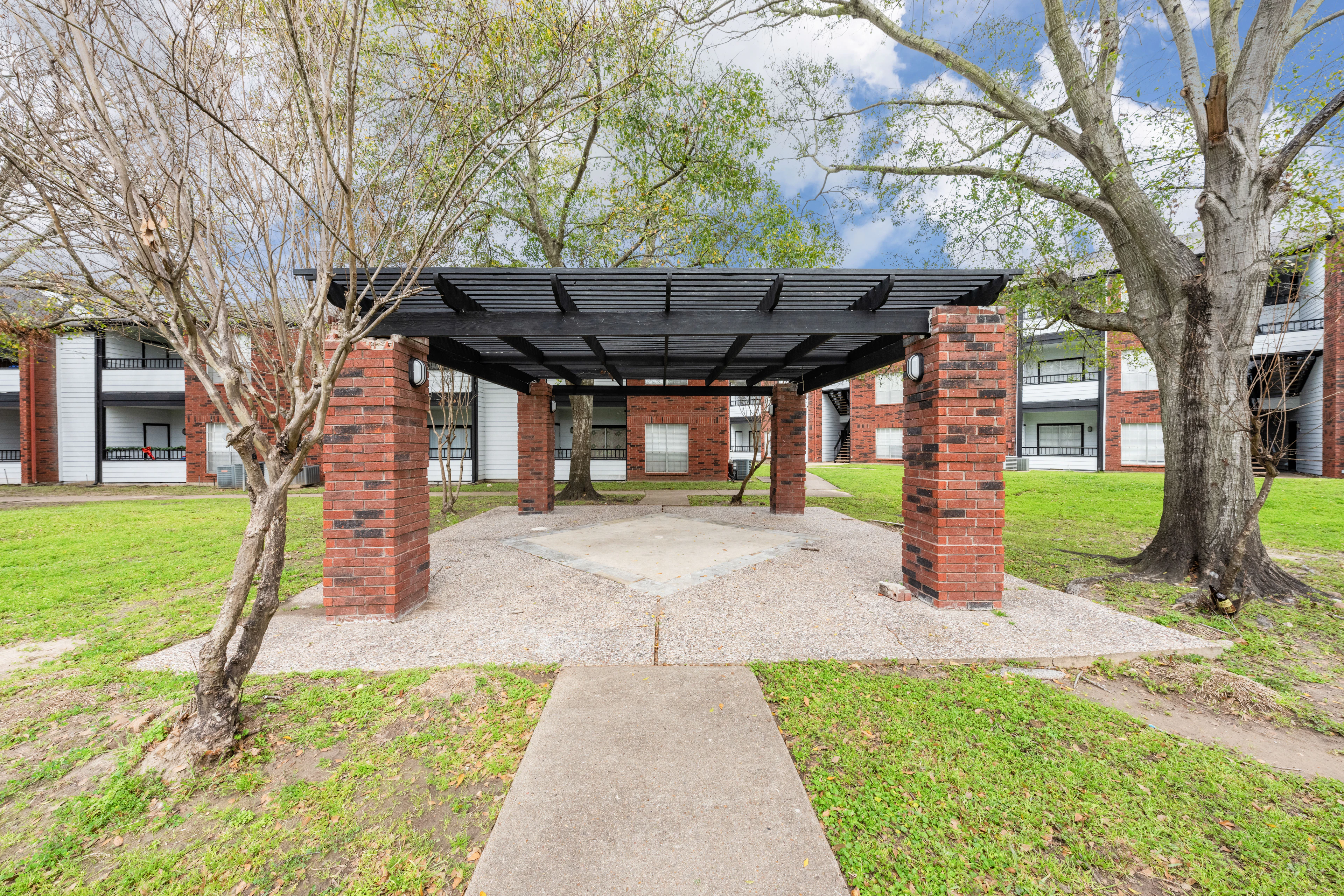 Outdoor covered patio area with ample seating, TVs, and grills with a city view at West Oaks Landing Apartments in Houston.